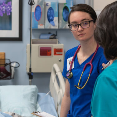 FRCC Nursing Student standing next to a gurney listening to a nursing instructor