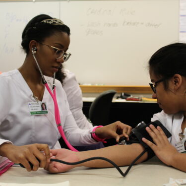 Two POC nursing students practicing taking blood pressure