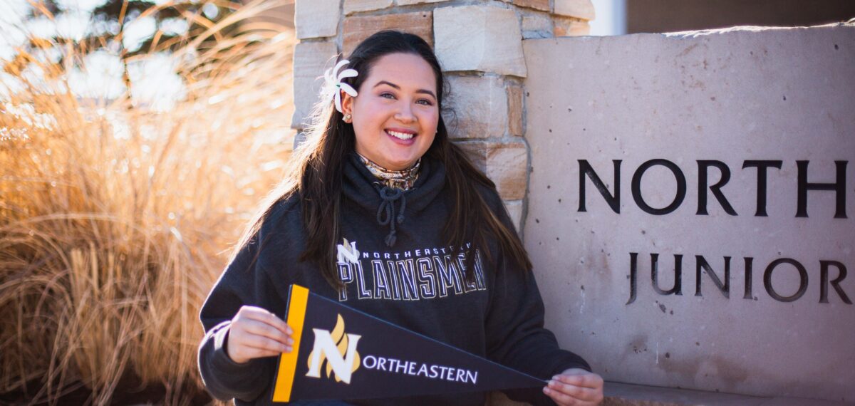 NJC Student Alexis Camara sitting in outside holding an NJC pennant