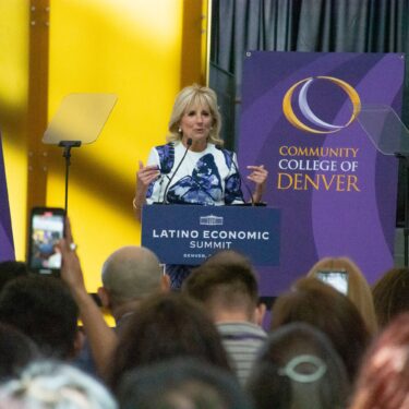 First Lady, Dr. Jill Biden, speaking at a podium with Community College of Denver banners in the background.